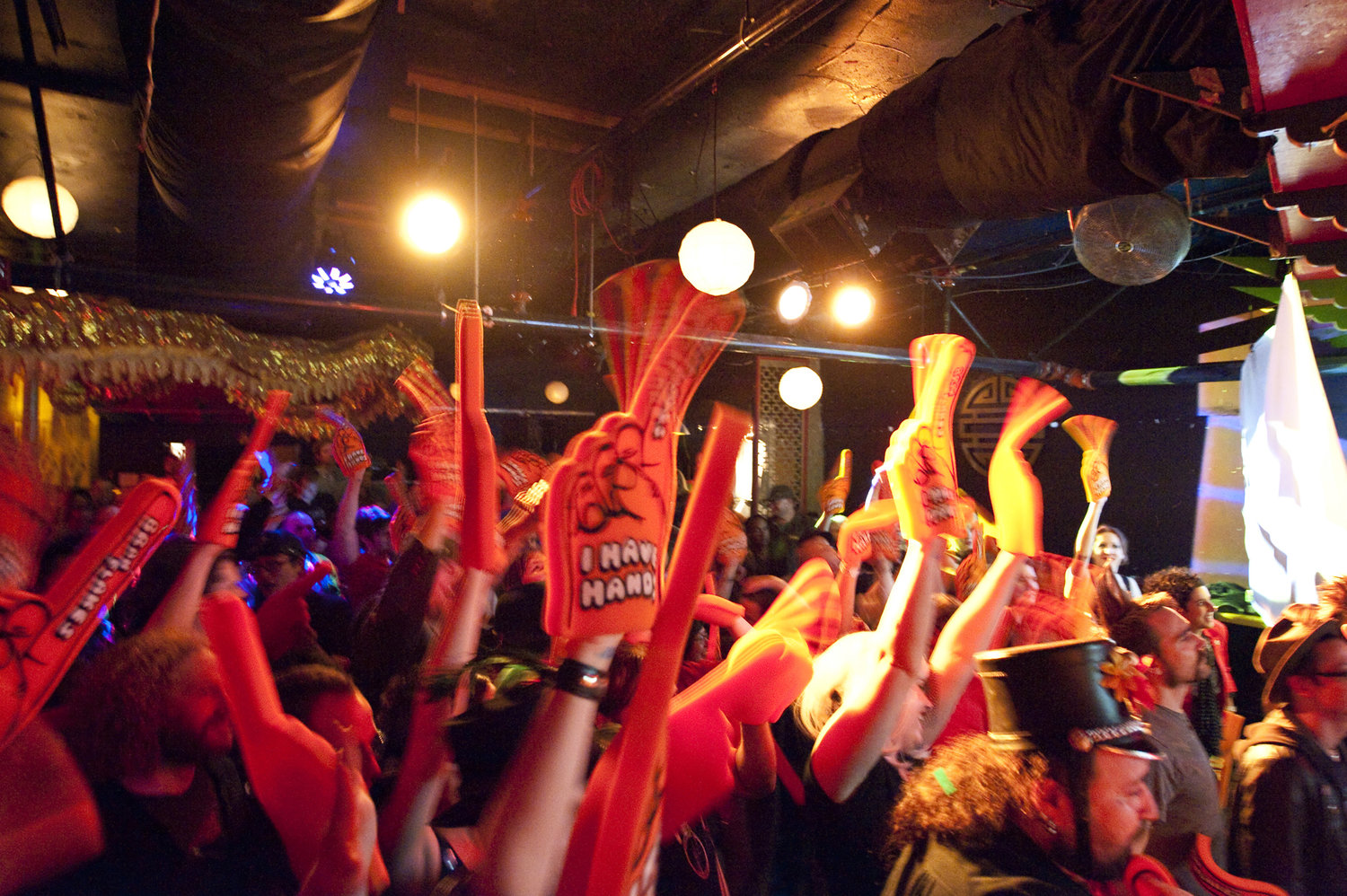 A shot of a crowd from one of their concerts. They are all waving orange foam hands that say 'I Have Hands' on them